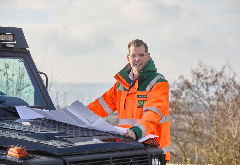 Vorstand Jan Deubig steht auf dem ZAK Gelände an einem Auto und schaut auf einen Lageplan